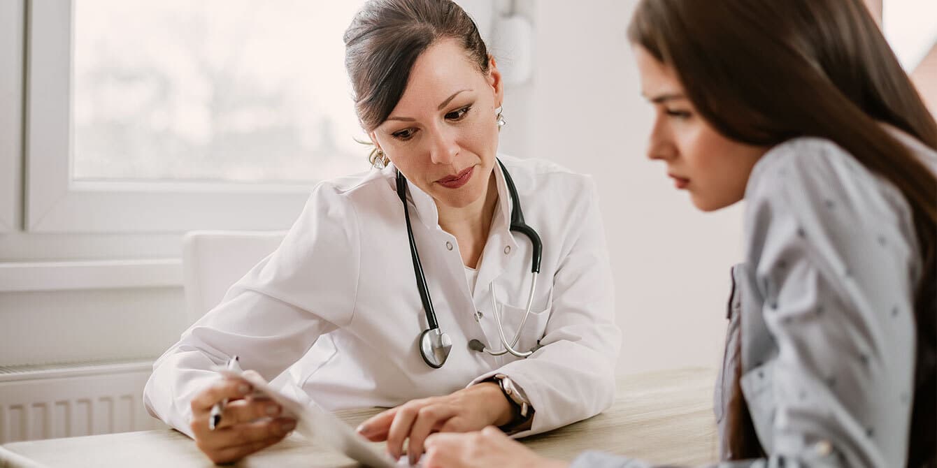 9 essential questions to ask at your preconception checkup Woman at preconception checkup talking with her doctor - preconception checkup questions to ask your doctor