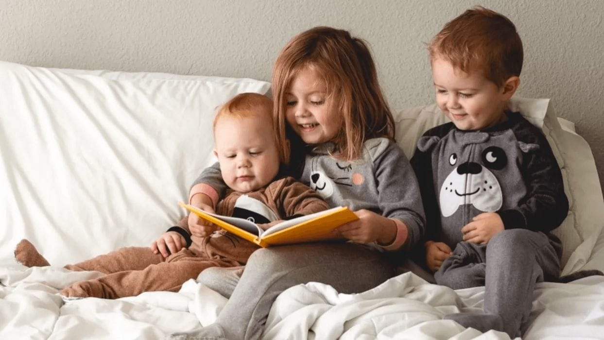 7 books to help kids celebrate all the winter holidays❄️ three kids reading on bed- winter holiday books