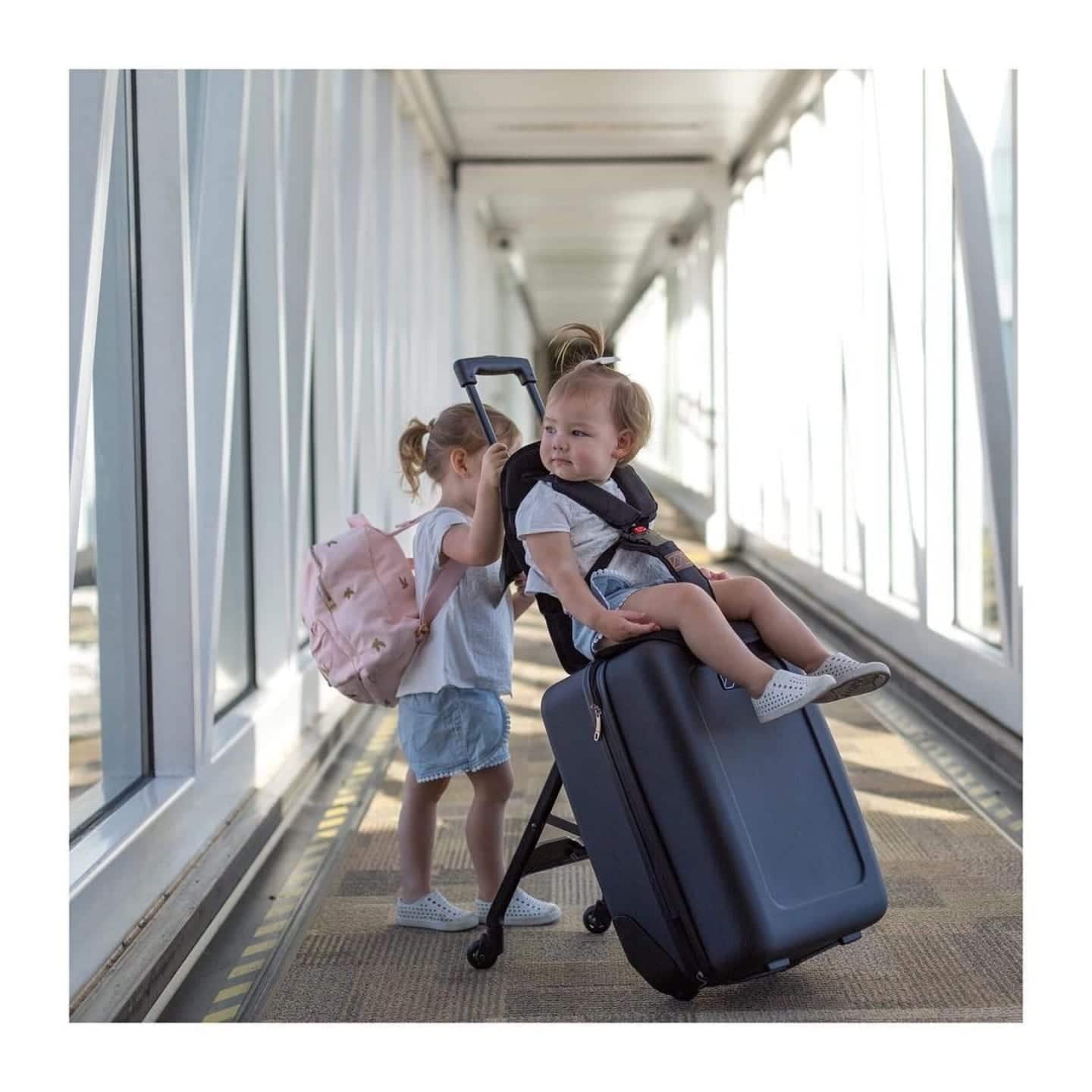 Baby’s first flight: Don’t leave home without these 15 must-haves ✈️ baby riding a suitcase at the airport, one of motherly's best products for baby's first flight