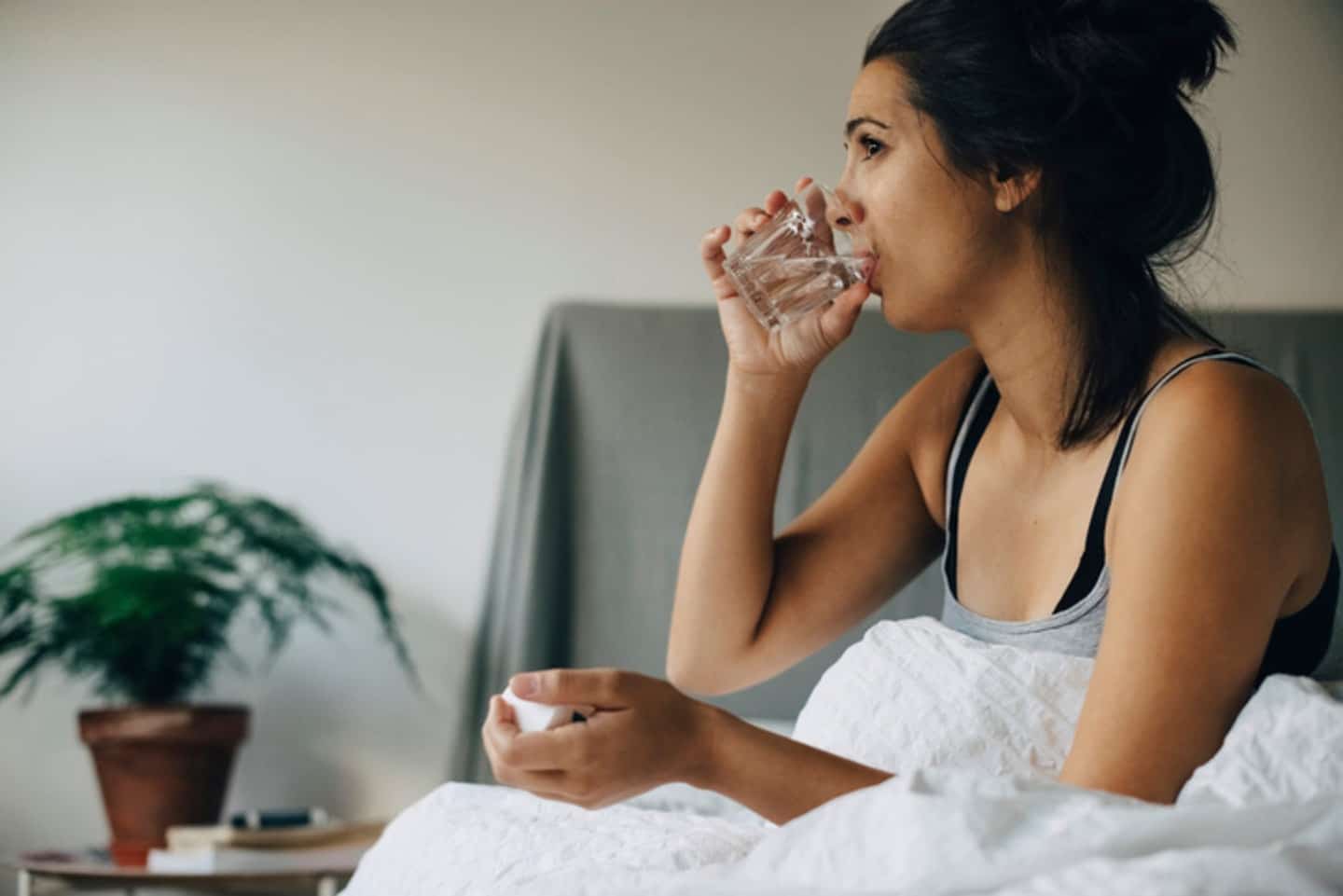 5 ways to manage nausea during pregnancy—naturally woman drinking glass of water sitting up in bed
