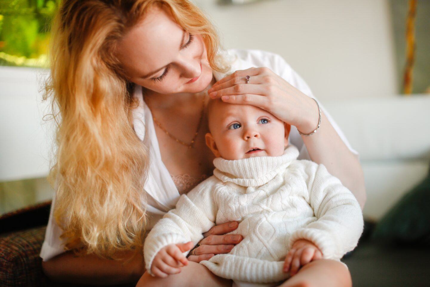 6 smart ways to stay healthy when your kids are sick mother with long hair holds baby on her lap and places hand on baby's forehead - how to stay healthy when kids are sick