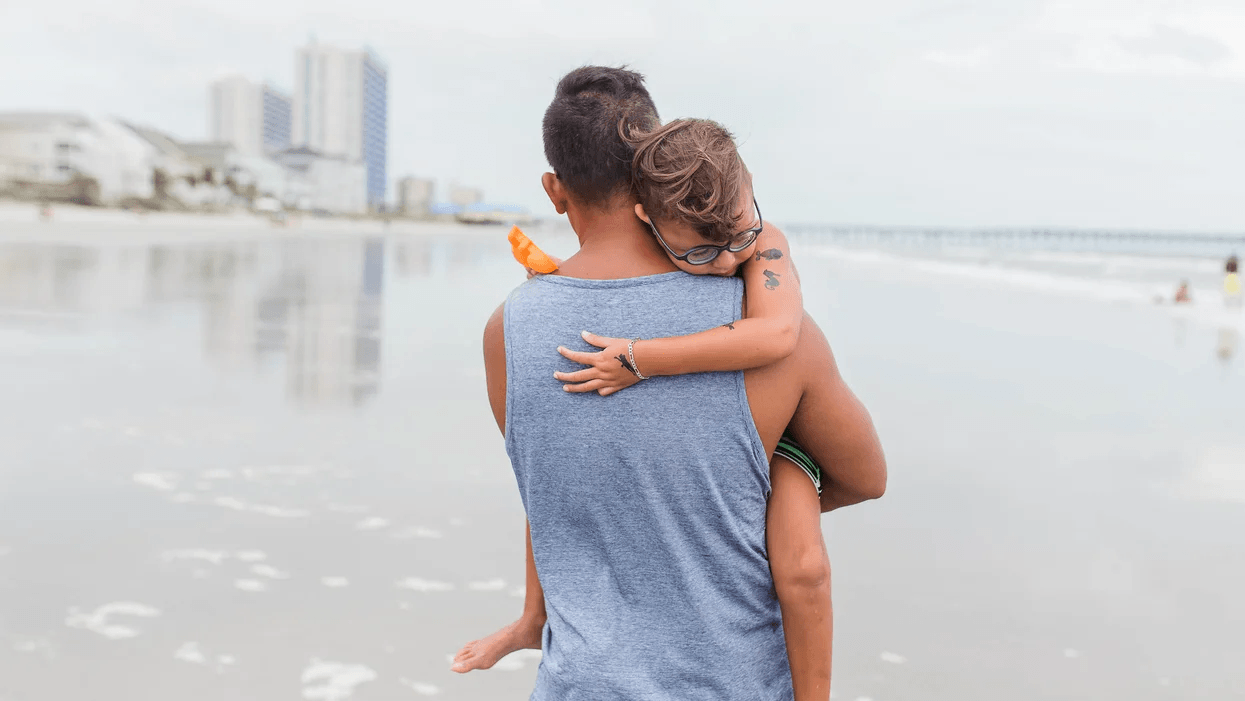 This is the year we finally recognize how much toxic masculinity hurts our sons dad carrying son on beach