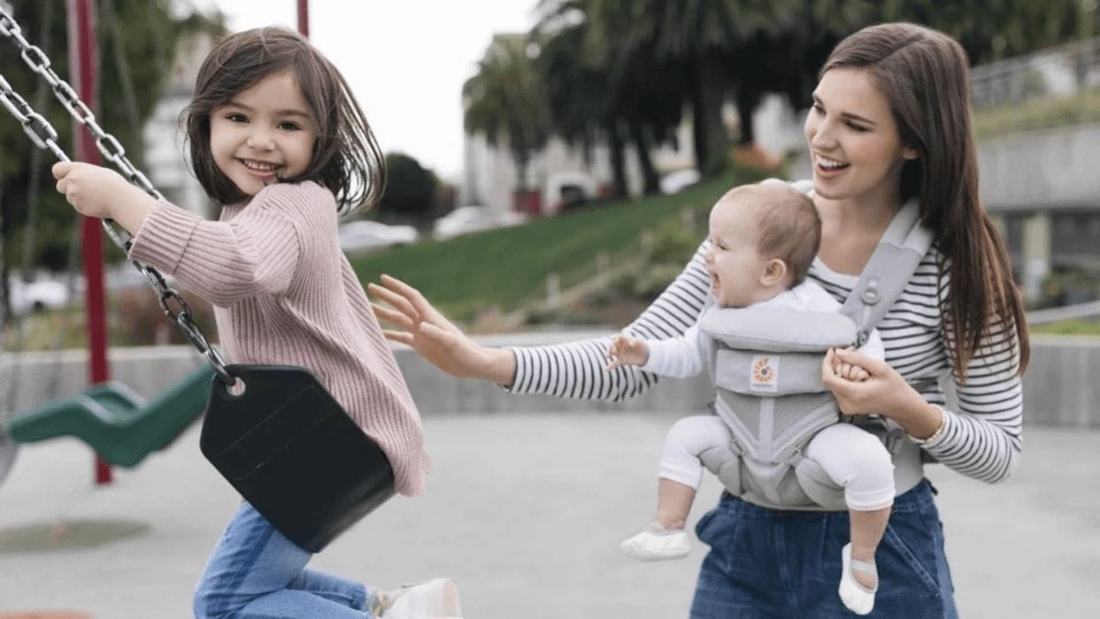 5 wins to celebrate during your first month being a mama of 2 đ mom wearing a baby while pushing a toddler on the swing