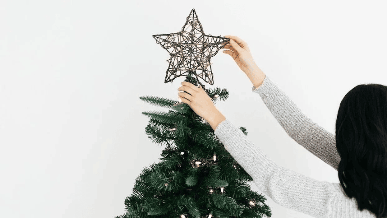 Yes, decorating for Christmas early *does* make people happy woman putting star on a Christmas tree- is it too early to decorate for christmas