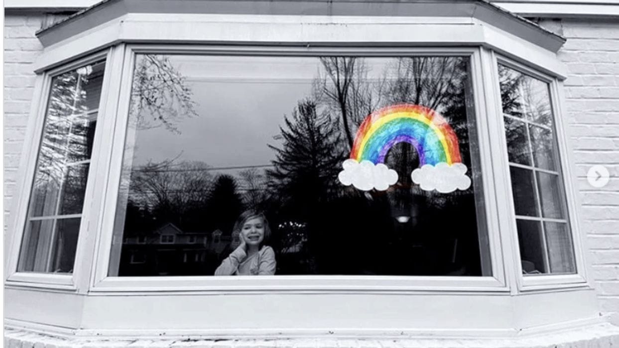 These kind acts are the light we need in the midst of the coronavirus pandemic little girl looking out a window with a rainbow drawing on it