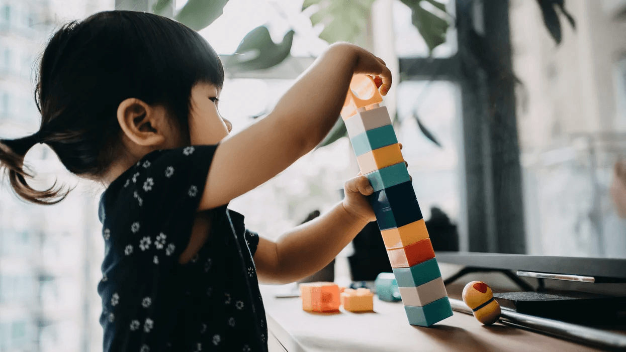 Teach basic math skills with these 15 easy math games for preschoolers little girl playing with stacking blocks