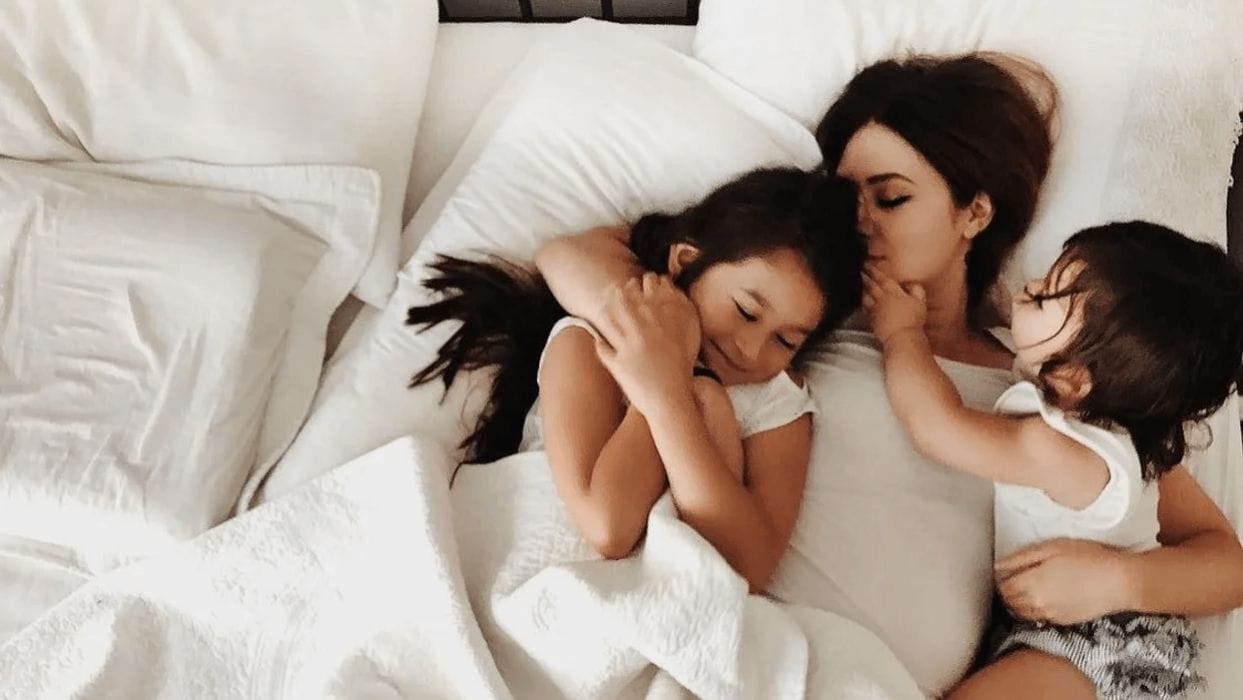 We need to stop shaming moms for co-sleeping—and research shows why mom cuddling two kids in bed