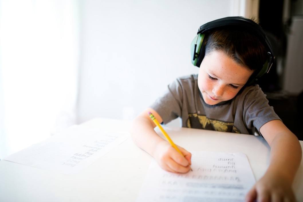 When will children go back to school? That depends on where you live young boy wearing headphones and doing homework on a table
