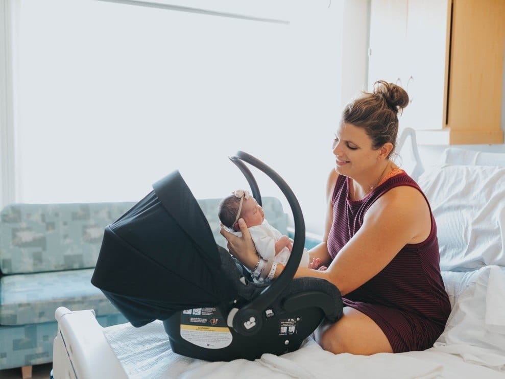 10 incredible products our editors wish they registered for the first time around woman sitting in a hospital bed putting baby in a car seat
