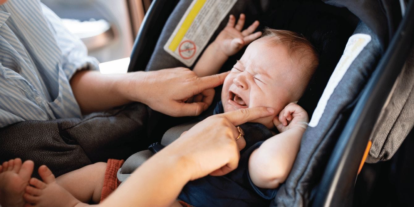 Here’s what to do when your baby hates the car seat mom trying to comfort her baby as it cries in a car seat
