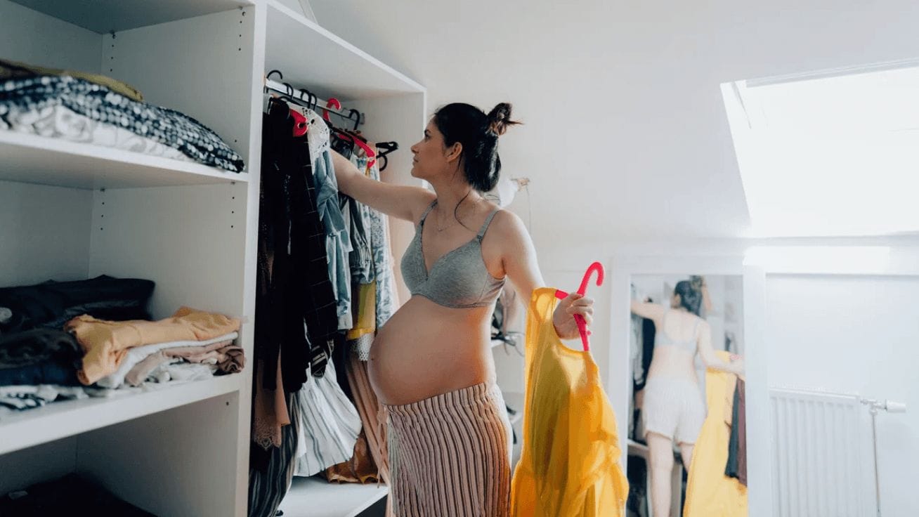 8 pieces your postpartum capsule wardrobe *needs* pregnant woman picking out clothes in a closet