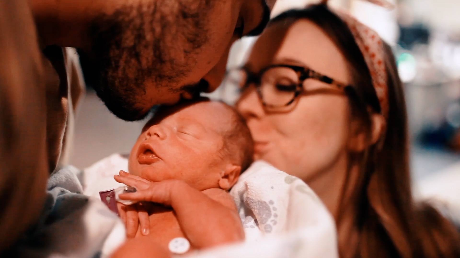 This is birth: First-time parents’ NICU journey parents kissing newborn baby on the forehead