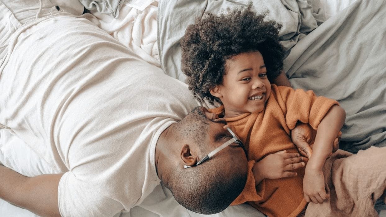 5 ways to calm your energetic child before bedtime dad playing with son in bed to calm child - how to calm your child