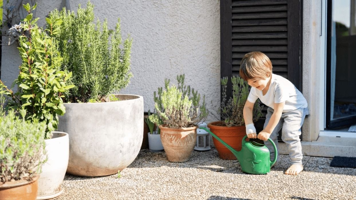 How to turn your backyard into a Montessori-inspired play space little boy trying to lift pale to water plants