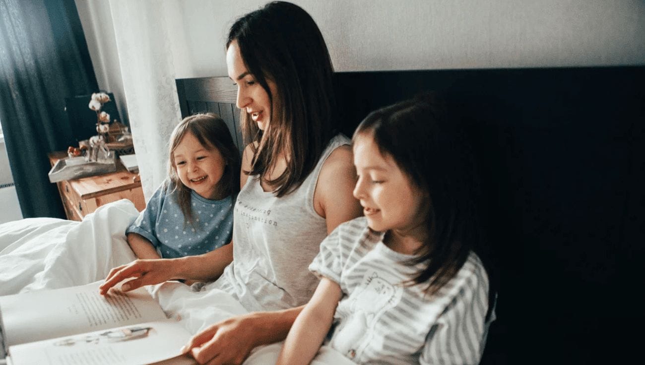 25 books about inspiring women to read with your kid for Women’s History Month mom reading with two girls in bed- books about inspiring women