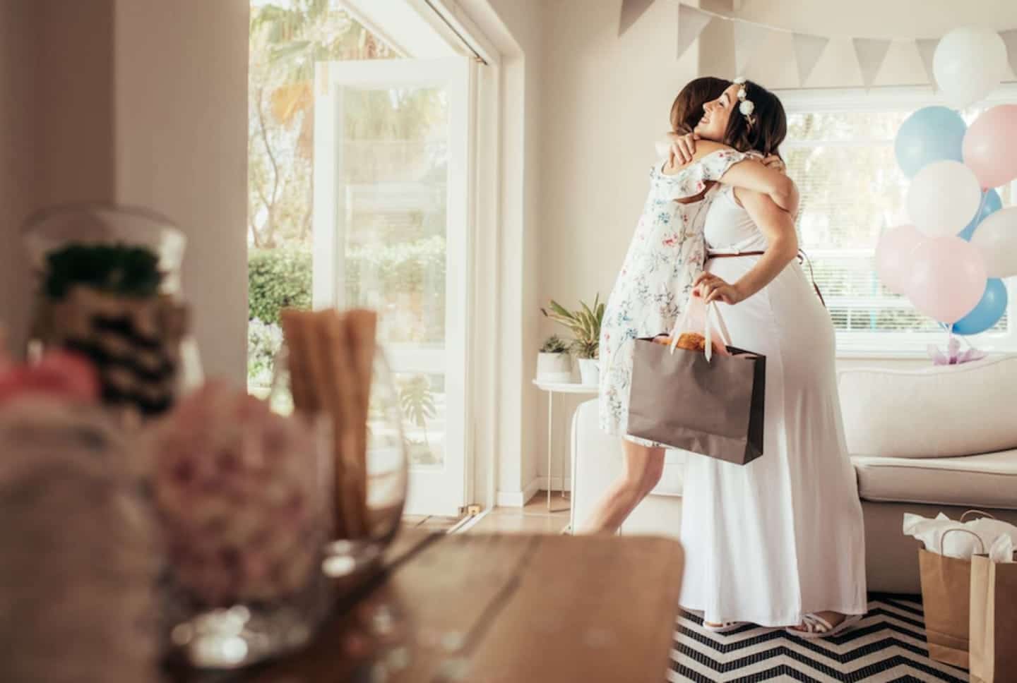 What to wear to a baby shower—whether you’re a guest or the mama-to-be pregnant woman hugging another woman and holding a gift