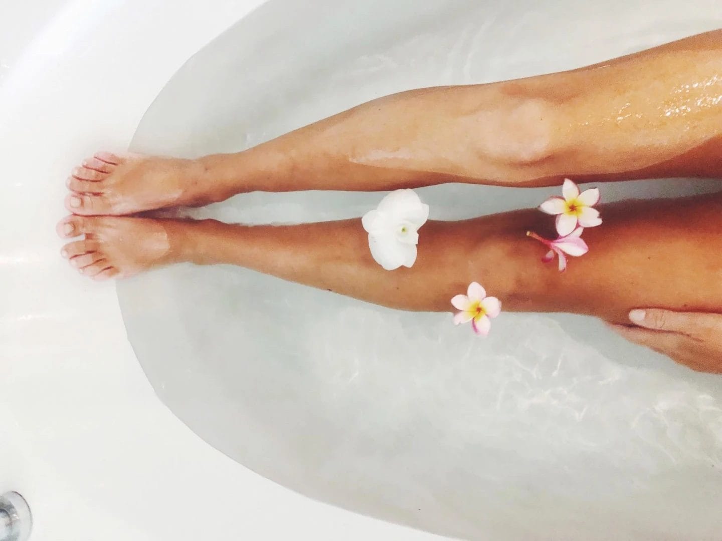 This is the best $7 you’ll ever spend on your skin hands-down woman's legs in bathtub with floating flowers
