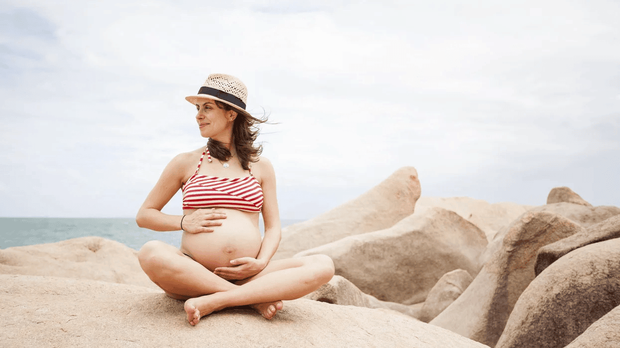 Summer pregnancy survival guide: Tips to stay cool & comfy pregnant woman holding belly on sand dunes