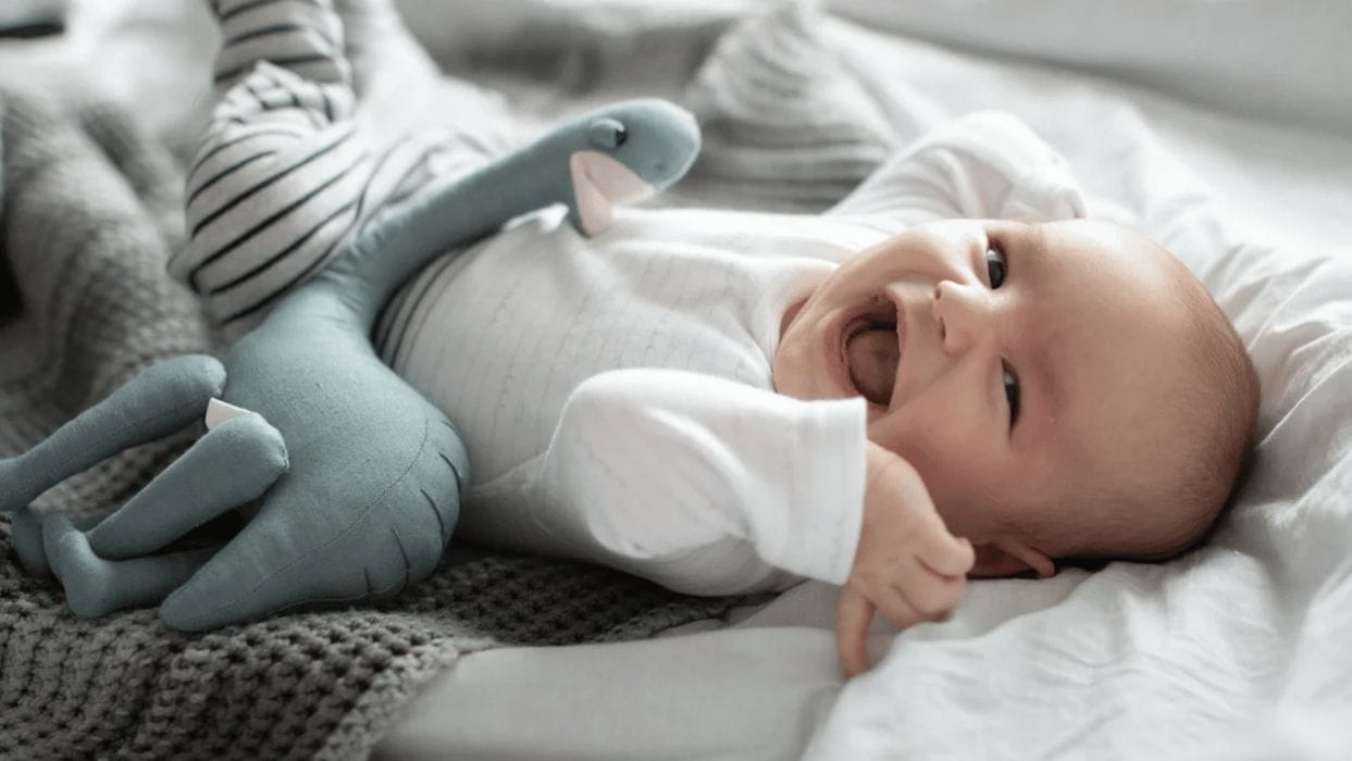 9-week-old baby feeding schedule & amounts baby laying on a bed and laughing - nine-week-old baby feeding schedule