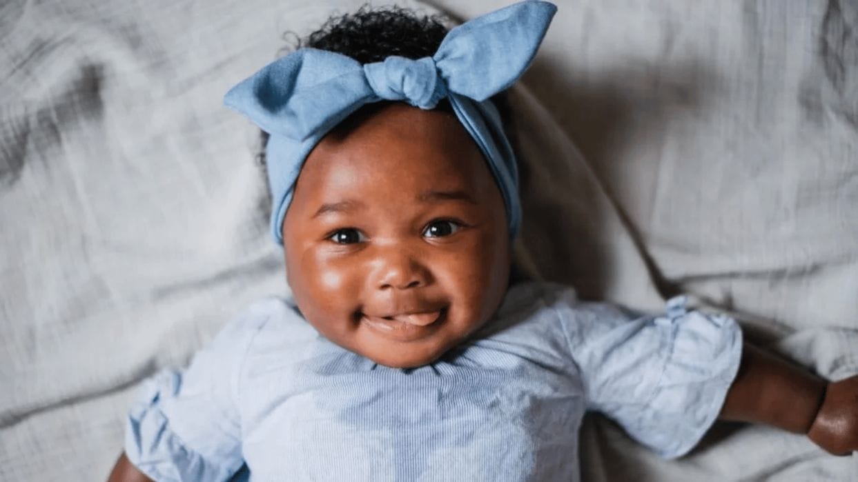 5-month-old baby feeding schedule & expert advice baby wearing a blue bow smiling at the camera - 5-month-old baby feedings schedule