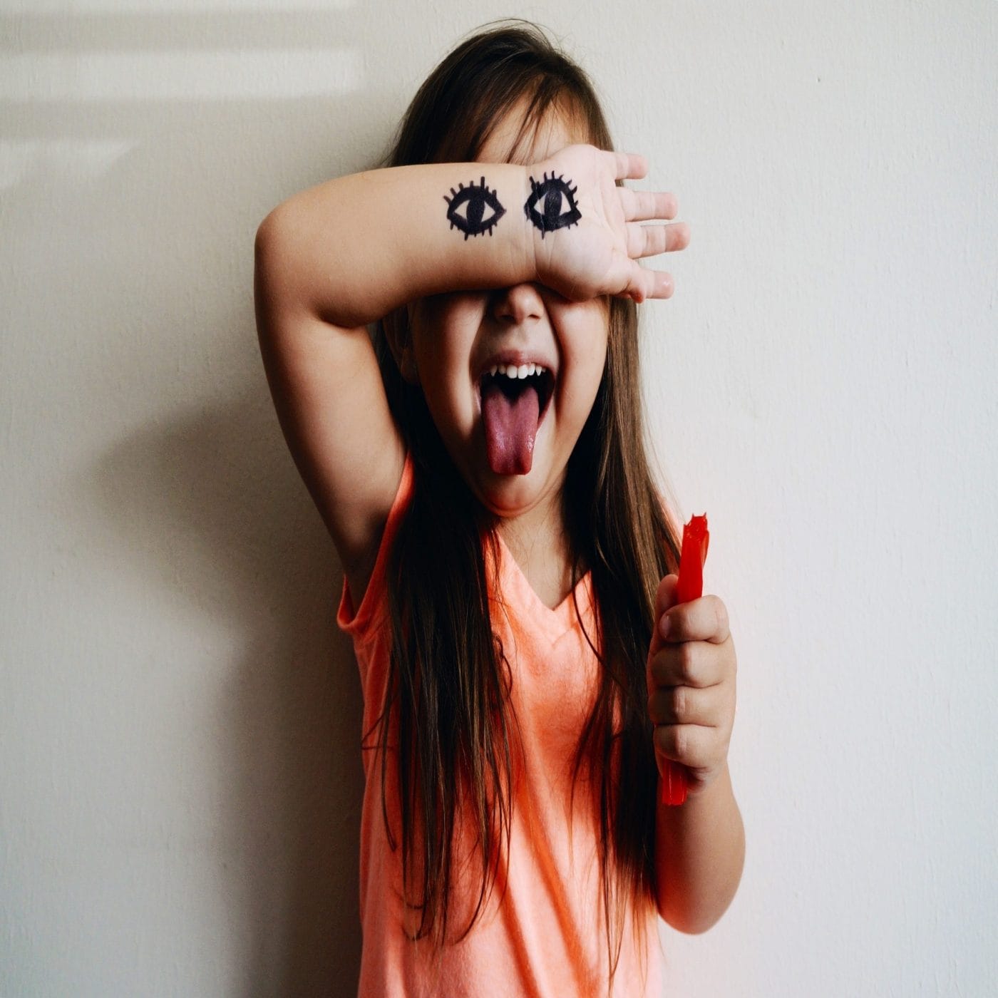 How my strong-willed child is changing me—for the better little girl with eyes drawn on her arms and giving a thumbs up