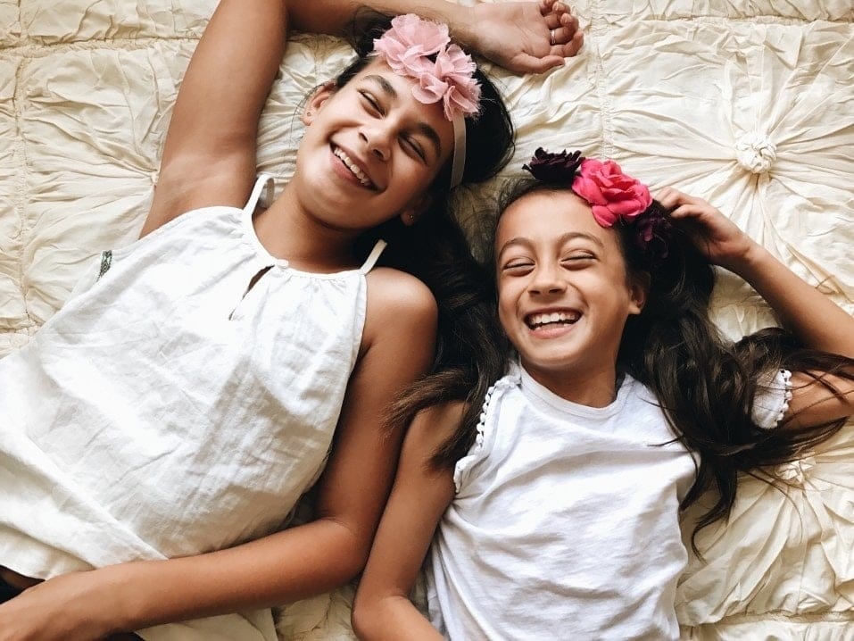 Cultivating gratitude is the key to happier kids (and adults, too) two girls wearing flower headbands lying down laughing- cultivating gratitude