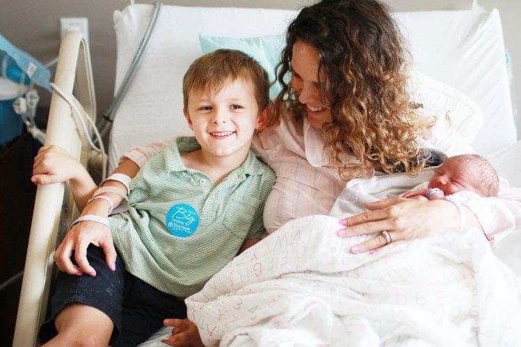 How your birth story can empower other pregnant mamas woman sitting in hospital bed with newborn and child