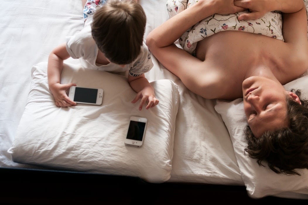 Screen time before bed means less sleep and higher BMIs for kids, says study child looking at a phone in bed screentime