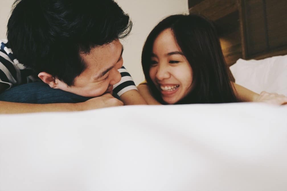 The one thing I wish I’d known about having sex after baby couple laughing on a bed together