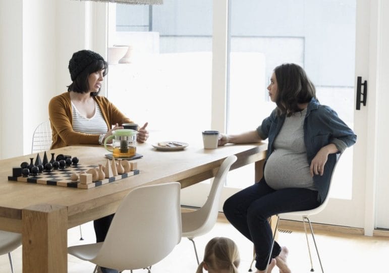 Not judging each other as mothers isn’t enough—here’s what else we need to do two moms sitting at a table together