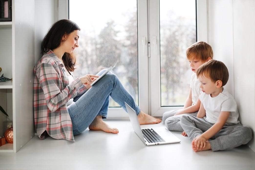 Social distancing for parents means empty playgrounds & canceled playdates mom sitting with two toddlers watching a computer screen