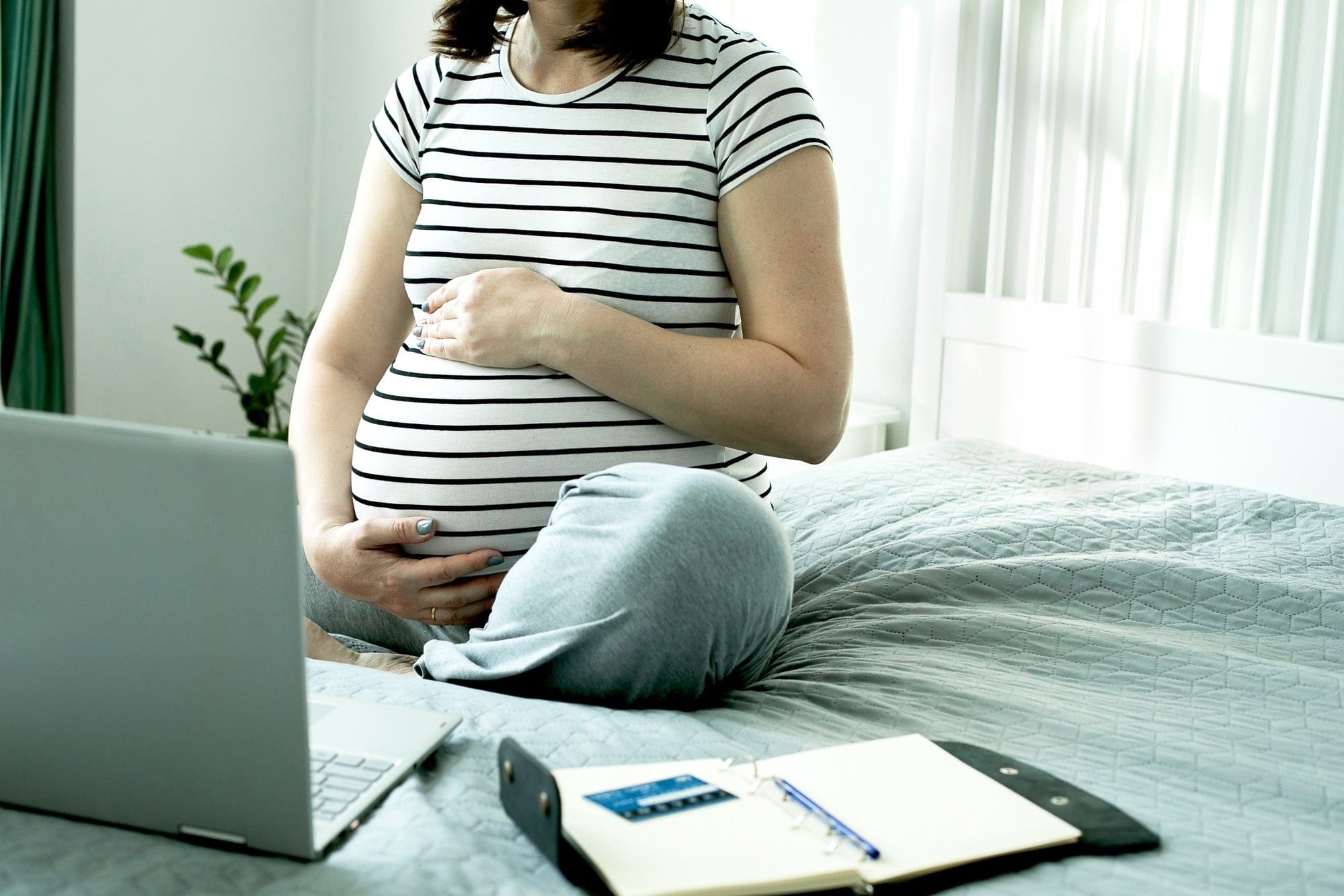 What you need to know about taking maternity leave during a global pandemic pregnant woman working in her bed