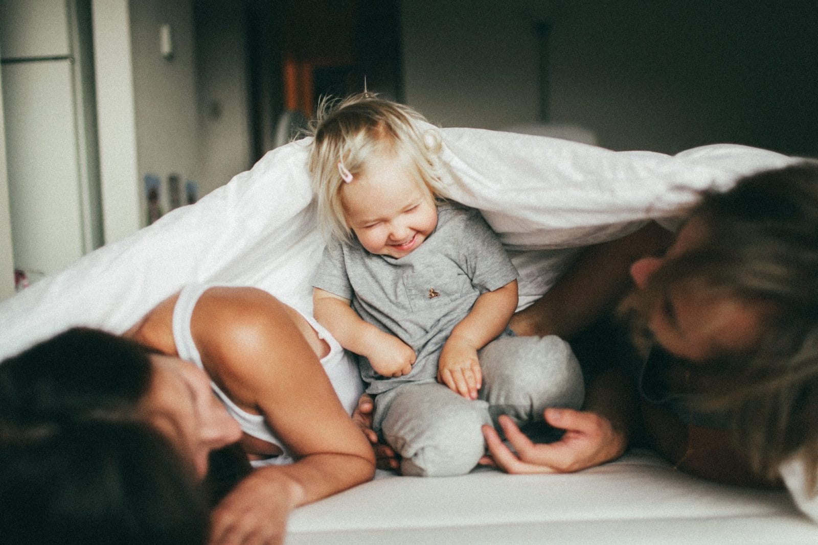 The world is starting to re-open, but I’m not ready to go back yet mom, dad and toddler playing on a bed