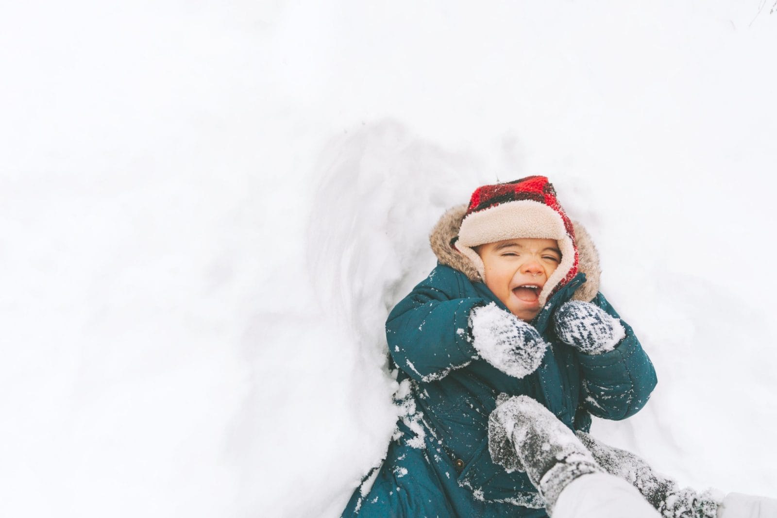 Cozy winter-inspired baby names for your little polar bear baby laughing and laying down in the snow- winter baby names