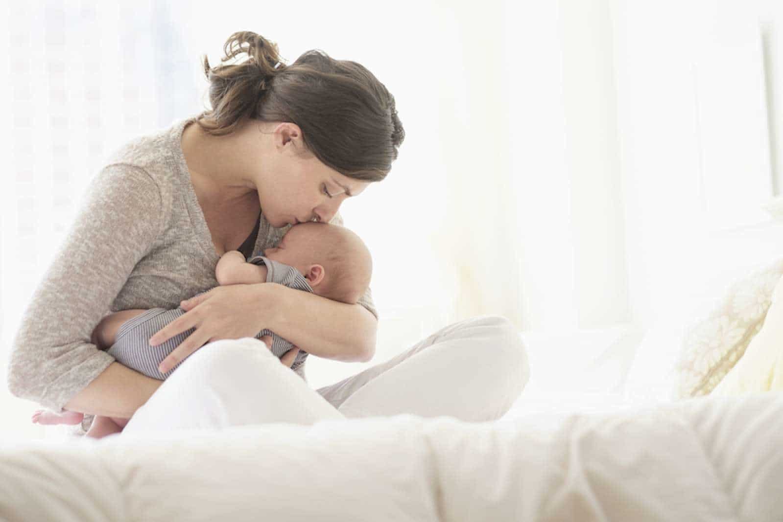 Singing to your baby is great for their brain development, says new study mom kissing newborn on the forehead, thinking about the benefits of singing to your baby