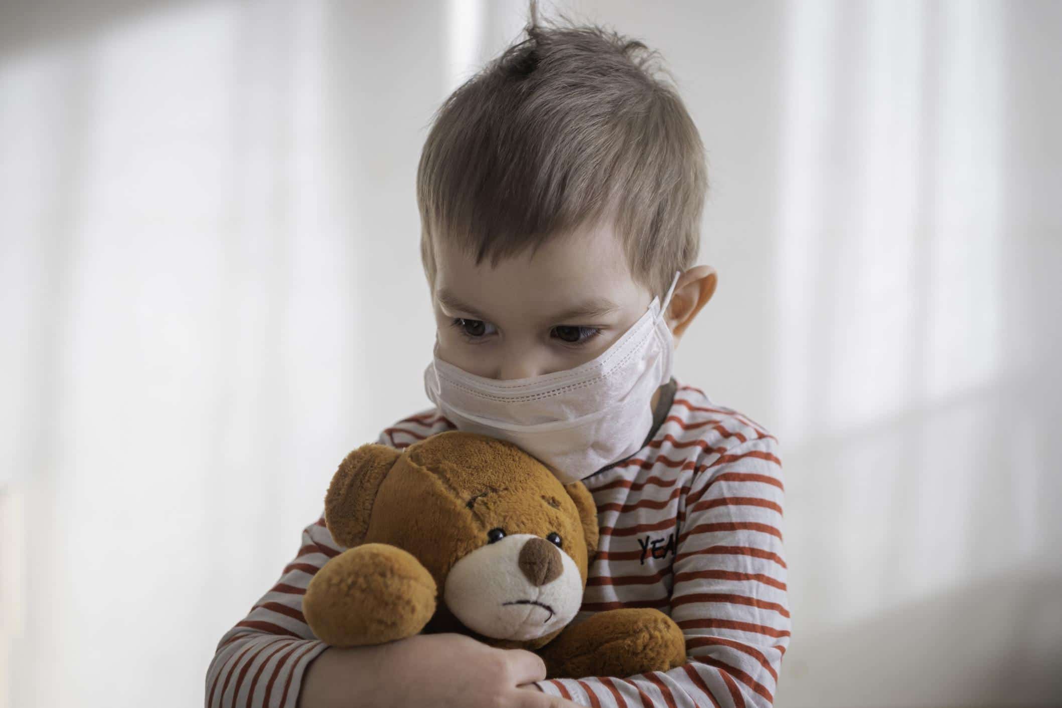 Babies and toddlers spread COVID more than teens, according to study toddler wearing a mask hugging a stuffed bear