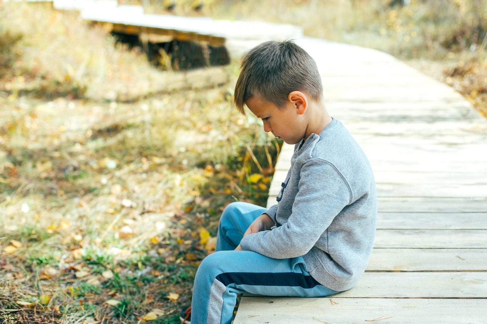 How to help your child deal with a bully, according to a child psychologist sad little boy sitting on a bridge - Motherly's tips for dealing with school bullying