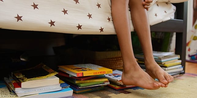 How to parent an introvert child sitting with feet hanging off bed, showing books stacked underneath bed - how to parent an introvert child