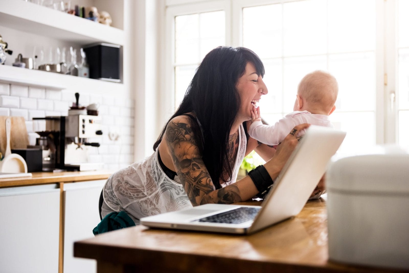 100+ mom jokes from some of the funniest moms on the internet mom laughing and telling a mom jokewhile holding baby on the counter