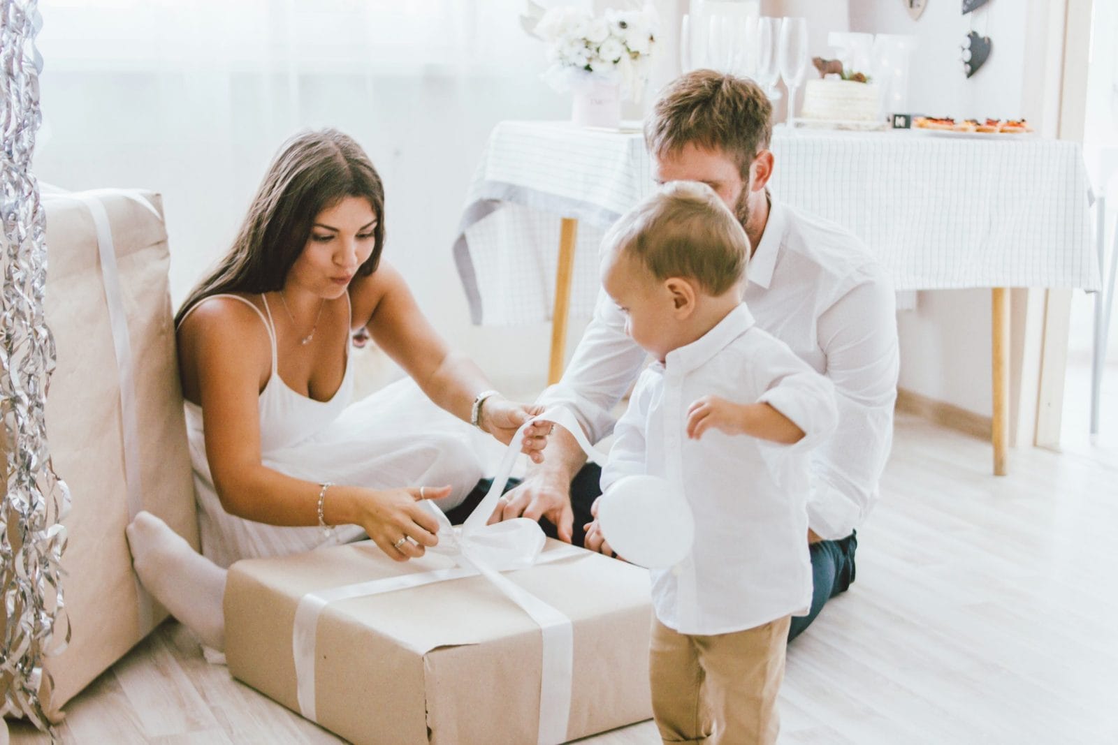 9 ways mamas can share the mental load this holiday season mother, father and child folding ribbon over a gift- holiday stress