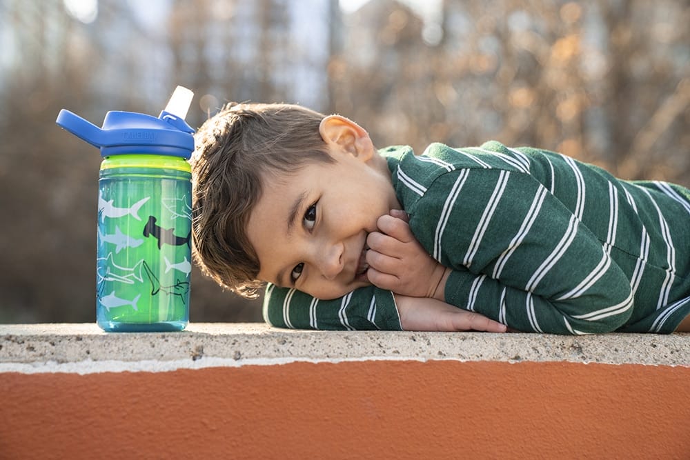 These water bottles make it so much easier to keep the whole family hydrated kid sitting at a park table with a water bottle