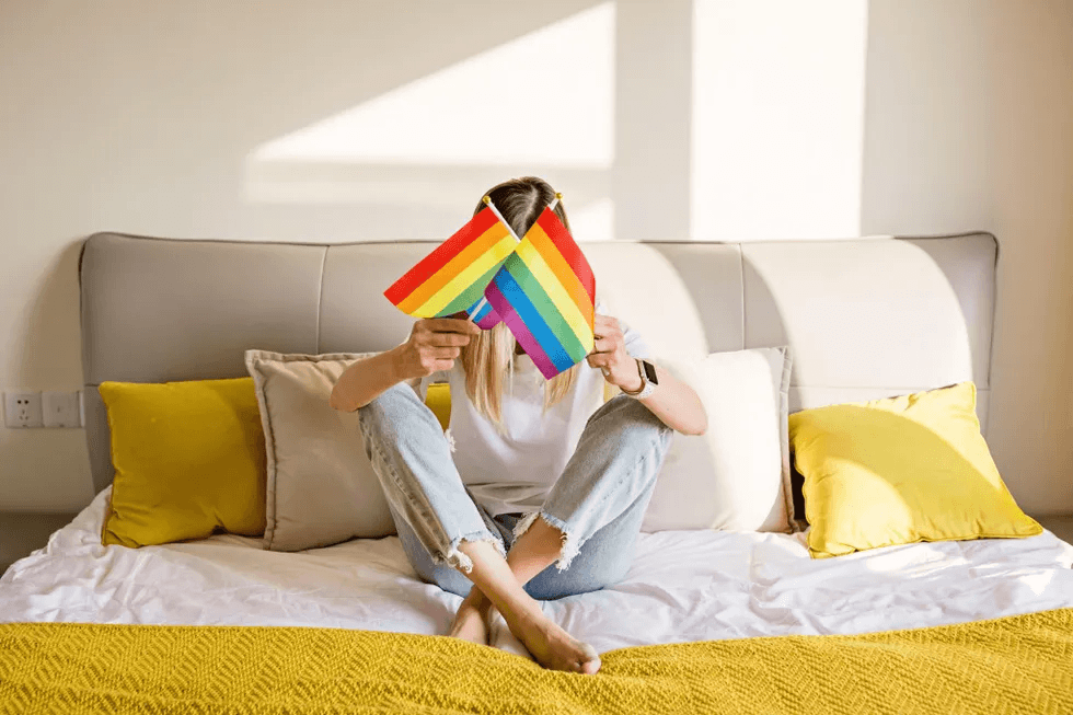 19 Pride-inspired products for the entire family that give back to the LGBTQ+ community woman sitting on a bed holding pride flags