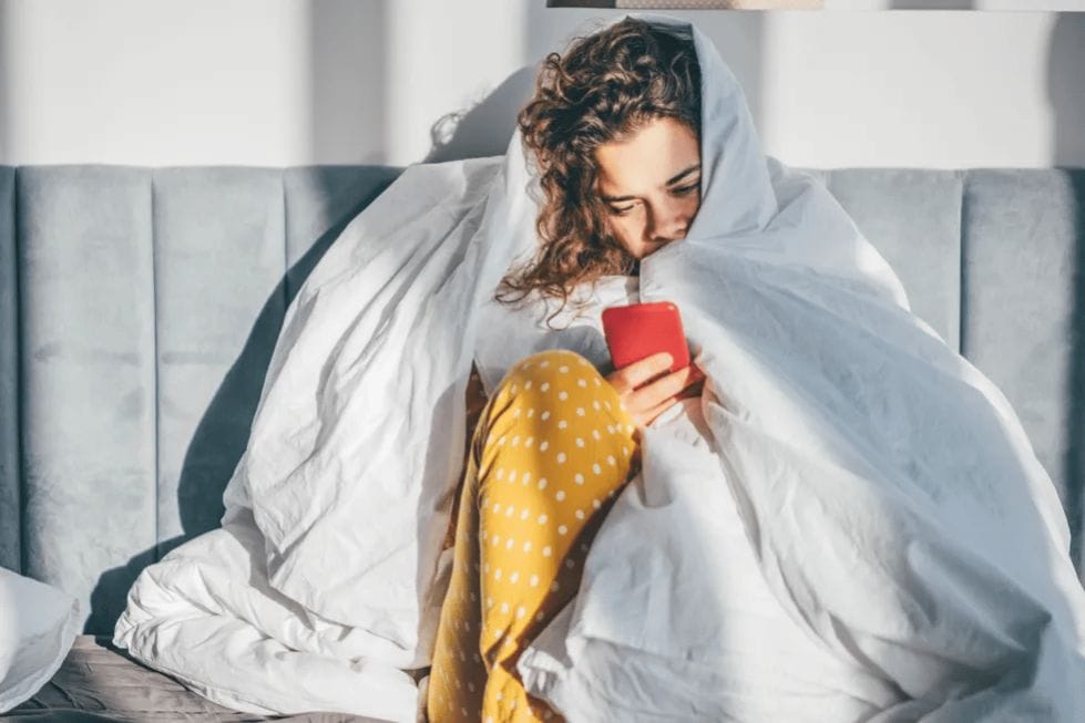 When does morning sickness start? woman-under-bed-covers-looking-at-phone