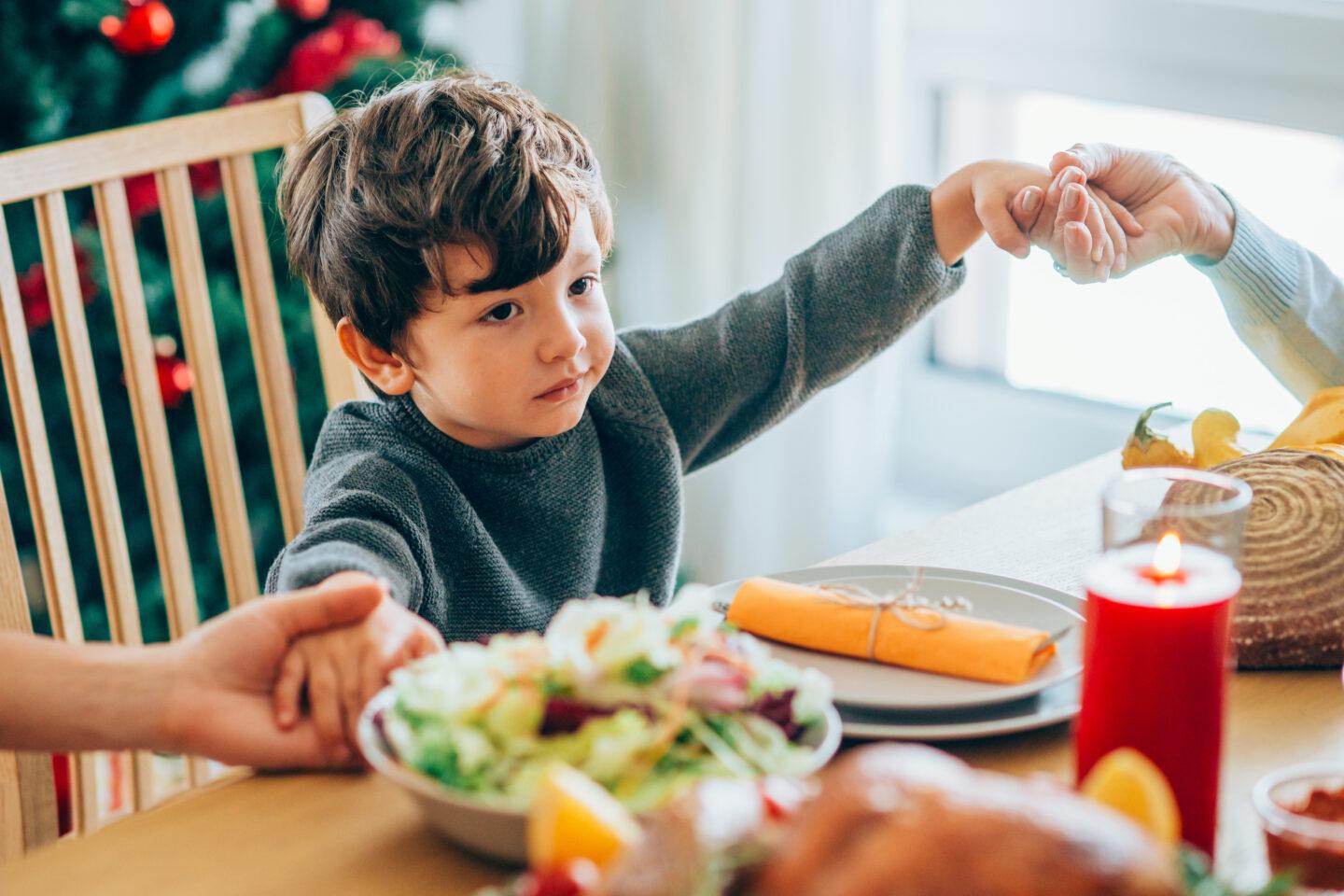 How to respect Indigenous history while celebrating Thanksgiving with your family little boy holding hands at dinner - how to celebrate thanksgiving respectfully