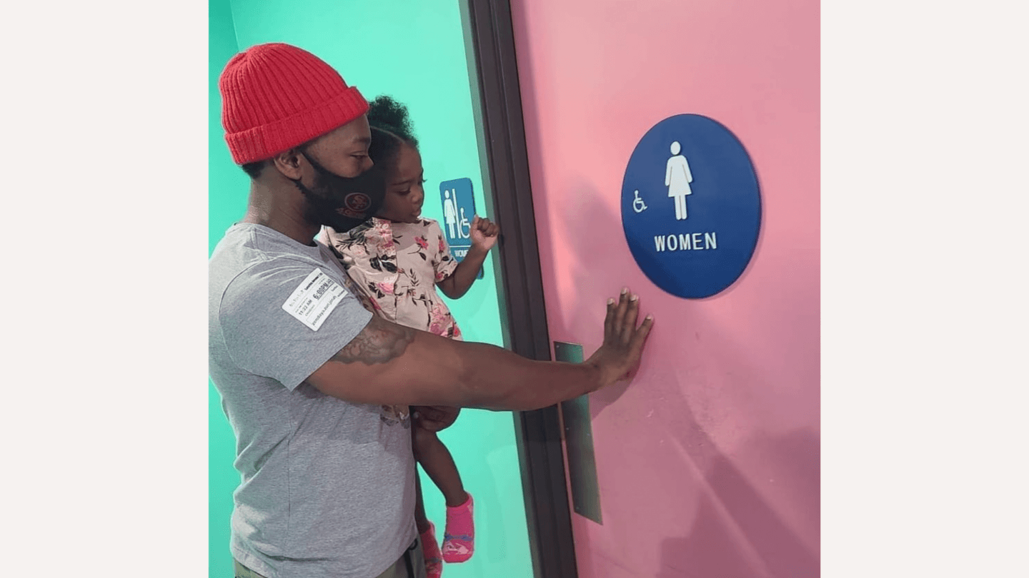 Dad’s viral post shows exactly why men’s bathrooms should be kid-friendly Dad holding baby girl in front of a women's bathroom