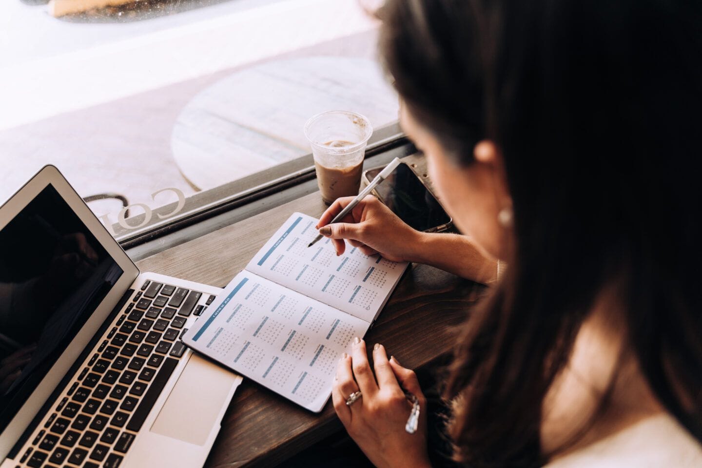 Is it implantation bleeding or your period? Here’s how to tell the difference woman writing in day planner at cafe with laptop and coffee - implantation bleeding postpartum