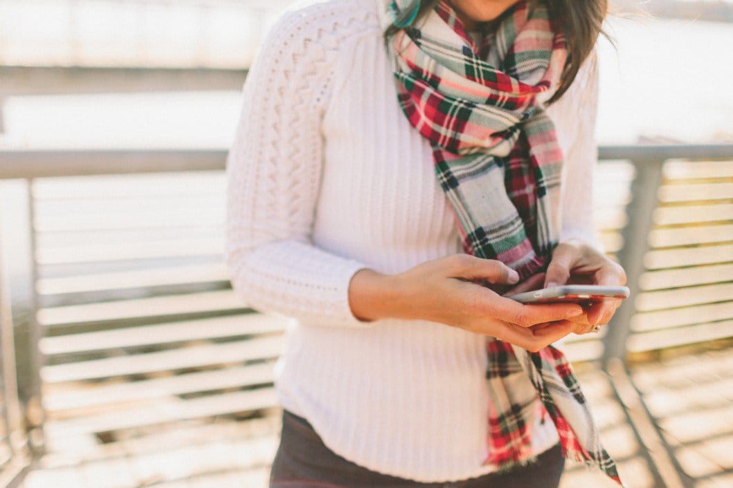 40+ digital and subscription gifts for the entire family woman in plaid scarf looking at her phone for best digital gifts