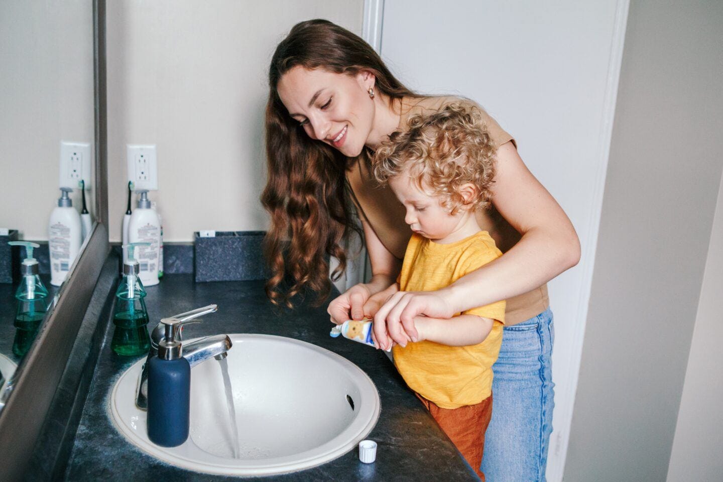 A little praise helps toddlers brush their teeth for longer, study finds Toddler fights tooth brushing: mother helping toddler brush teeth at bathroom sink