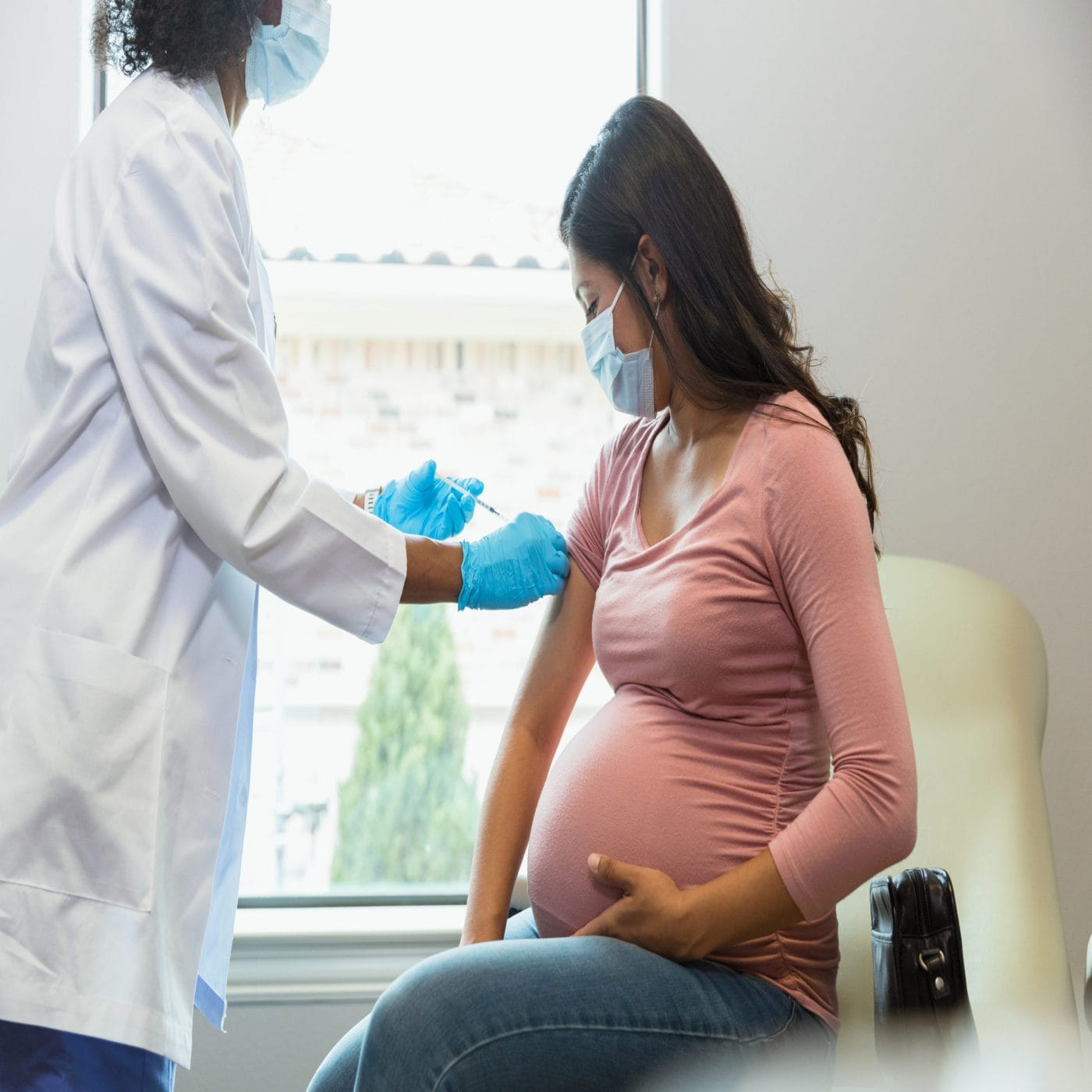 When is the best time to get the Covid vaccine or booster during pregnancy? covid vaccine in pregnancy: pregnant woman watches as a doctor administers a covid booster shot