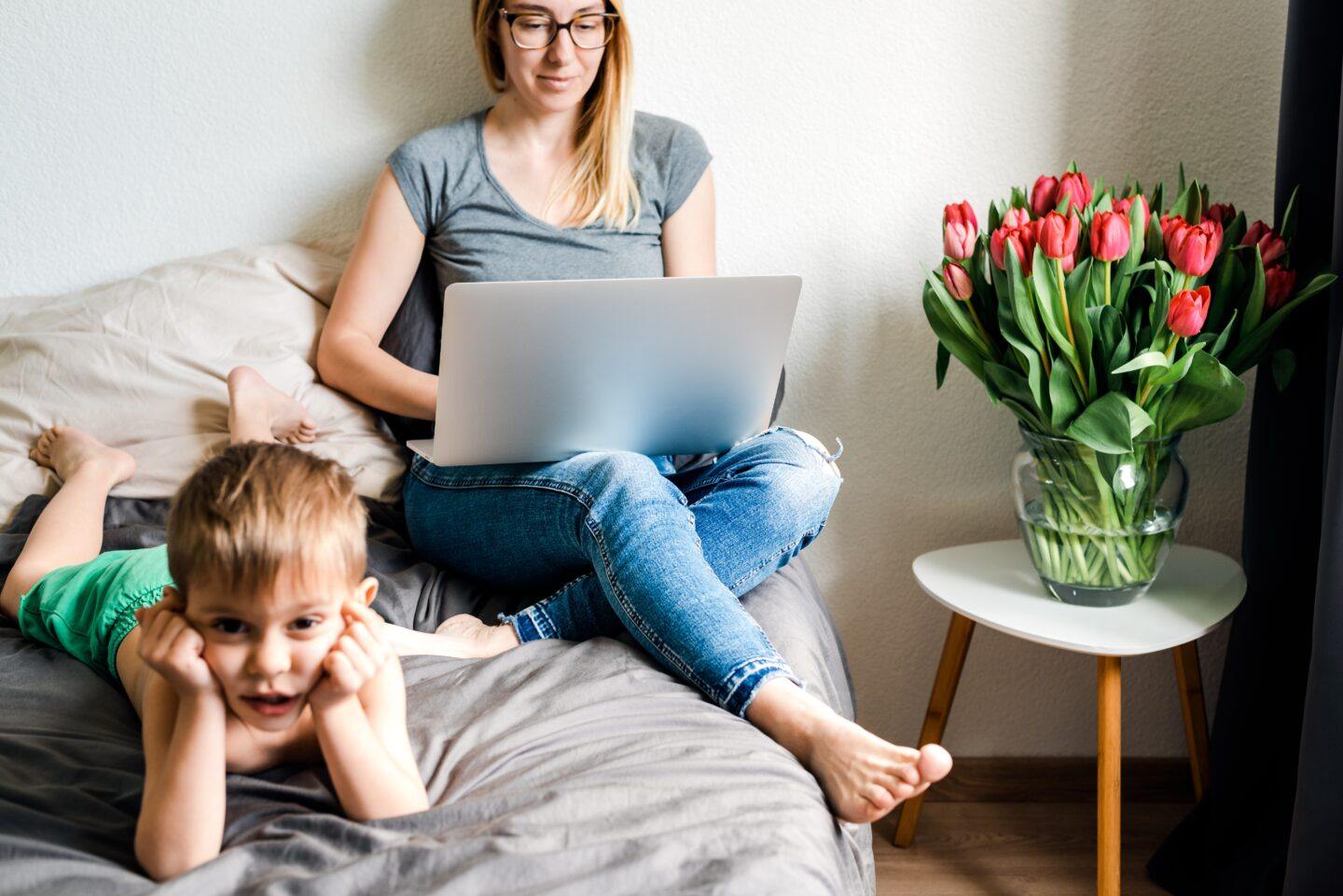 Being a working mom is my identity. But can we drop the label? mom working on laptop with toddler on the bed